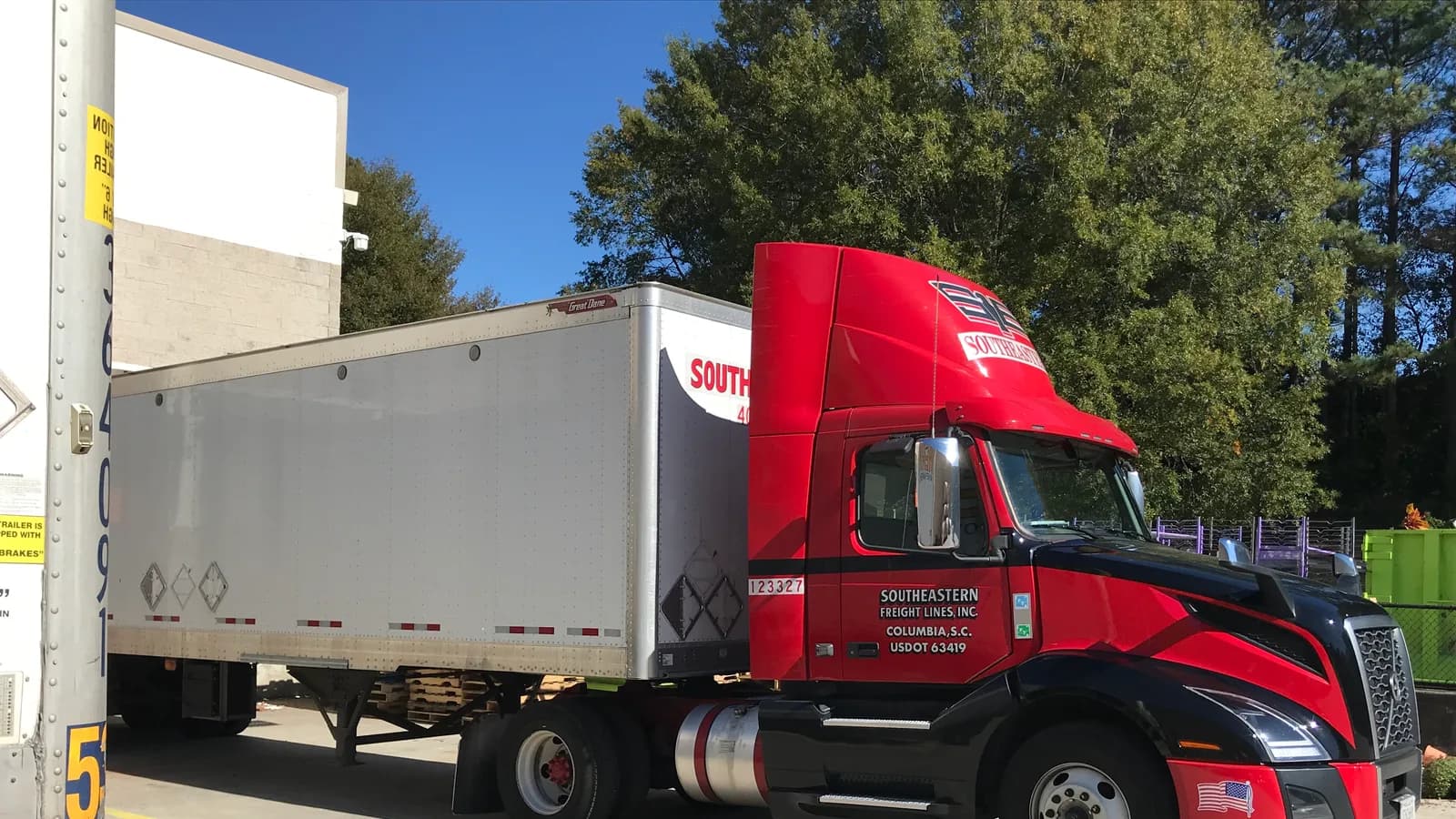 A red semi tractor with a dry van trailer parked at a loading dock