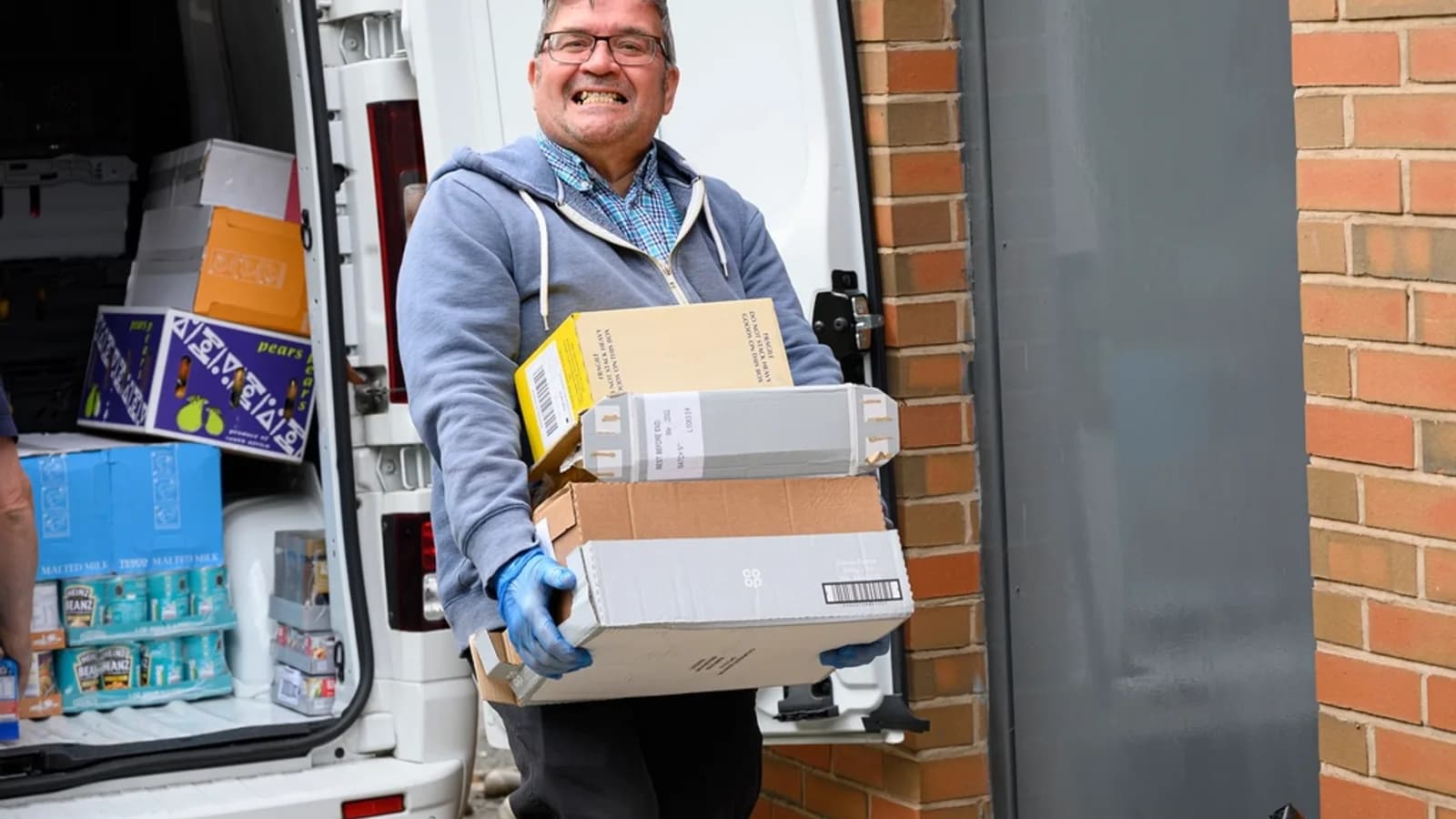 A delivery driver carrying boxes from the side door of a van to a front door