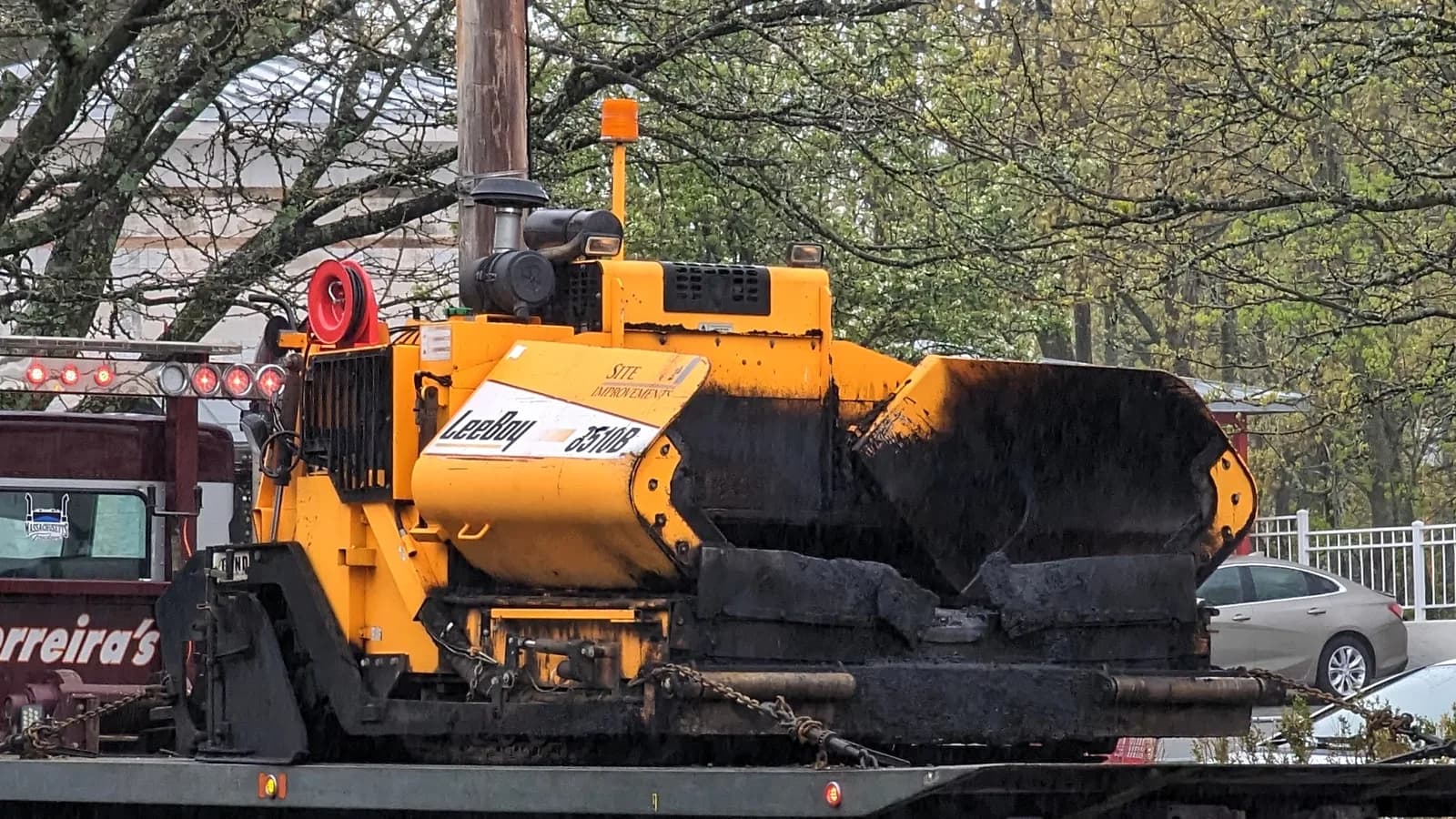 An orange asphalt paver laying a new road surface on a residential street