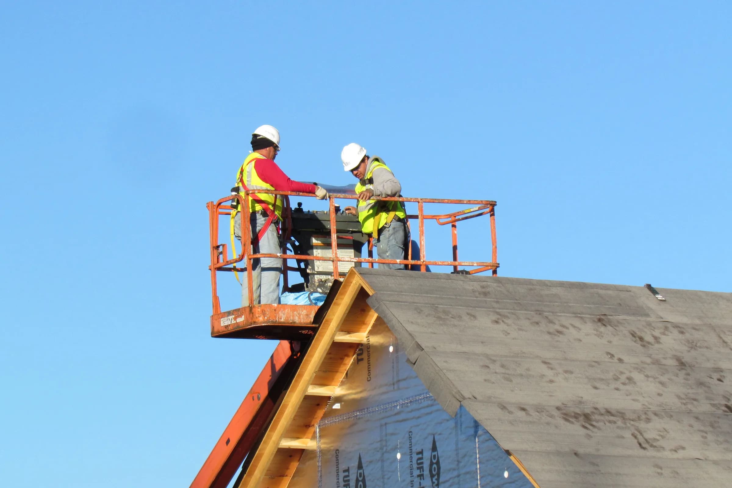 A roofing crew on a lift platform at the edge of a roof under construction