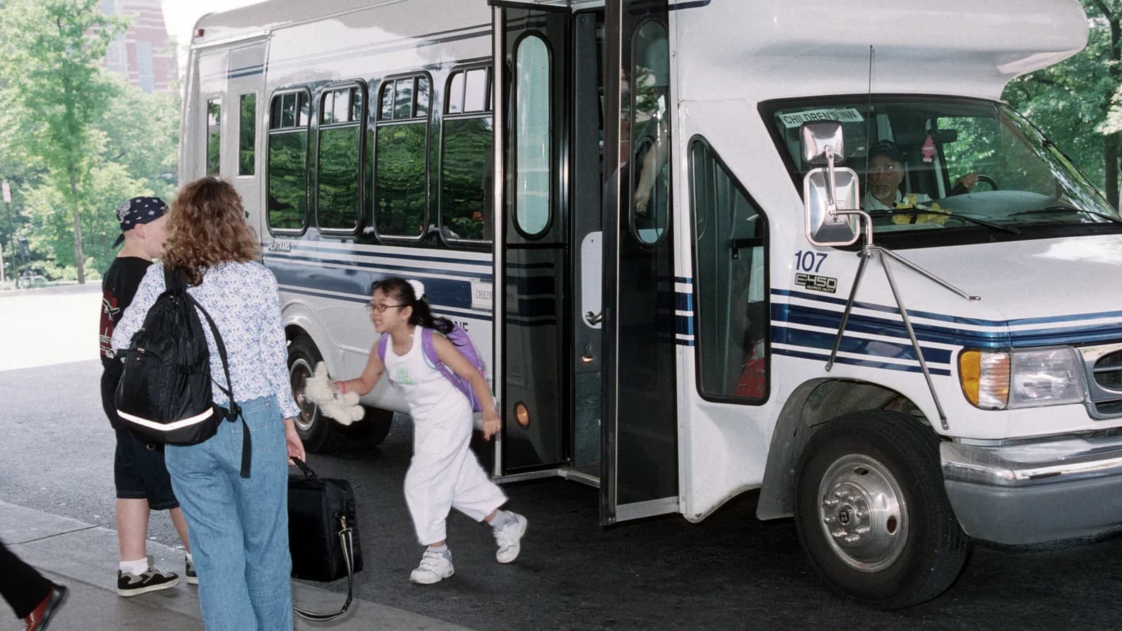 Students boarding a white campus shuttle bus at a stop