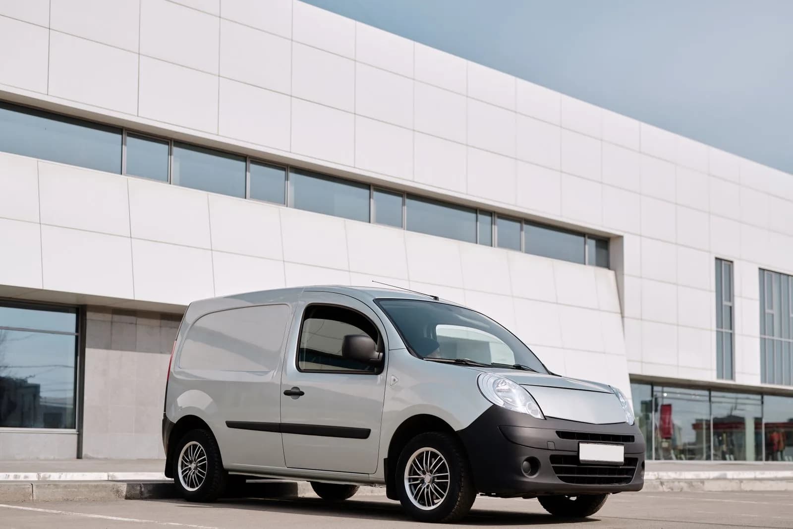 A small white service van parked outside a commercial building
