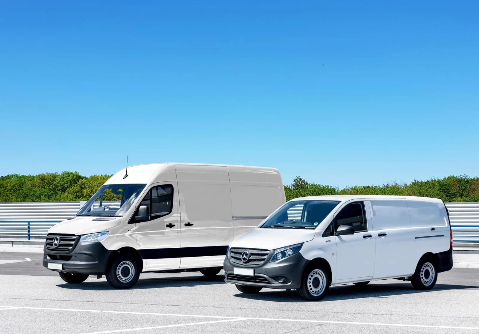Two white commercial vans parked side by side on a paved lot on a clear day